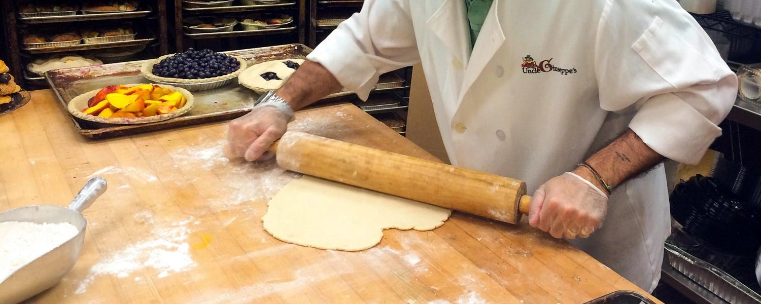 A man in a chefs coat rolling out dough