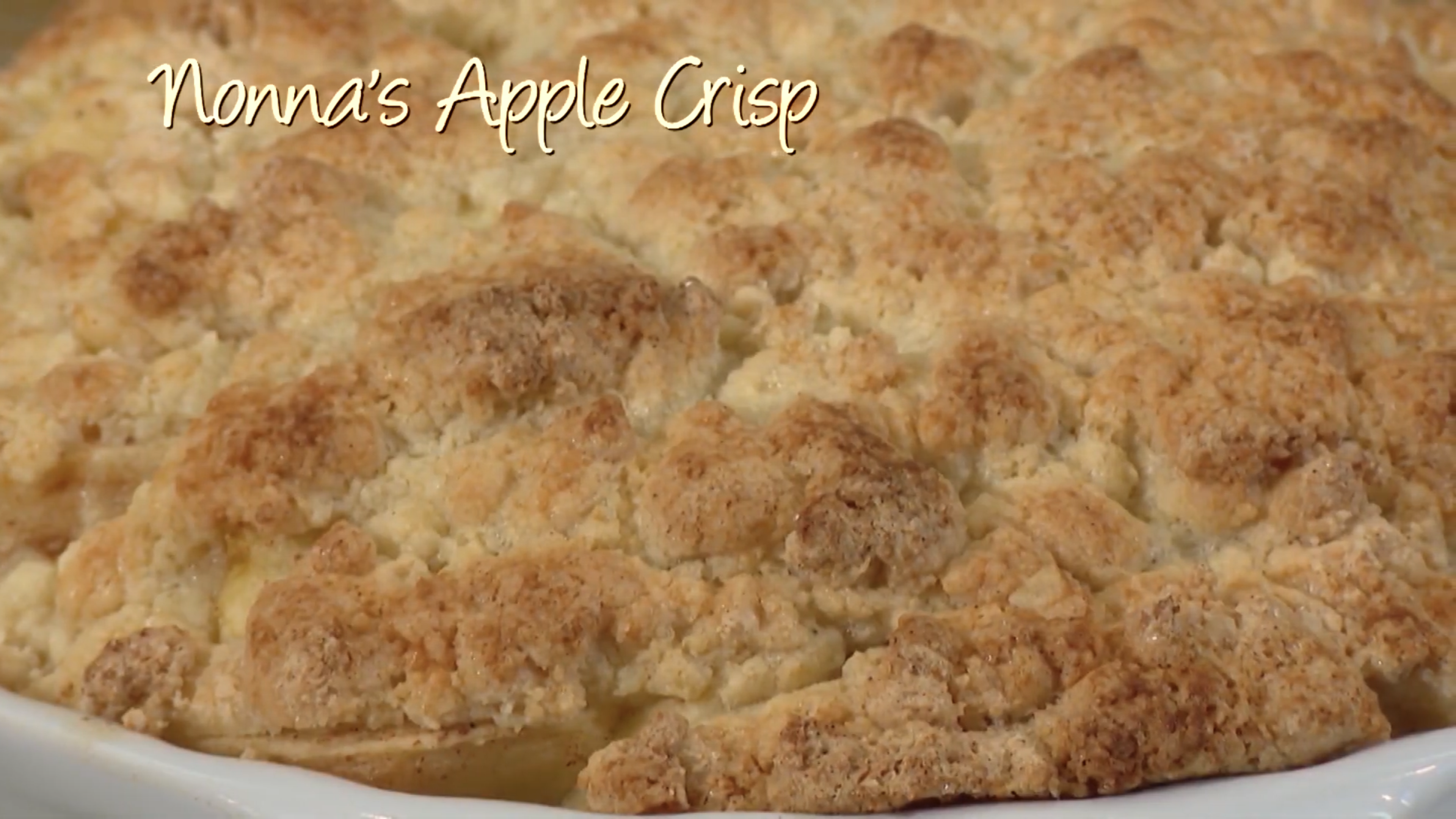 Close up shot of baked apple crisp in a white dish with "Nonna's Apple Crisp" written on it