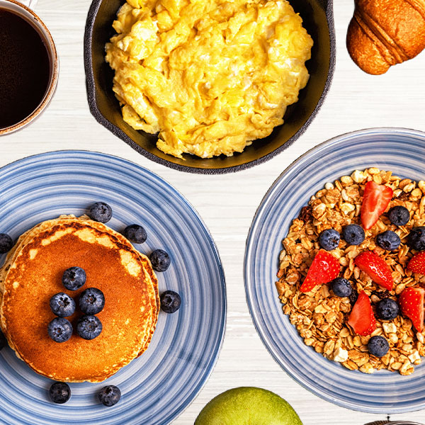Flat lay of scrambled eggs, pancakes and granola on white wood