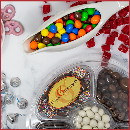 Gravy boat filled with m&ms and Uncle Giuseppe's candy platter on a white background with candy scattered